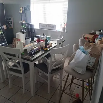 Dining table covered with bags, boxes and household items before cleaning