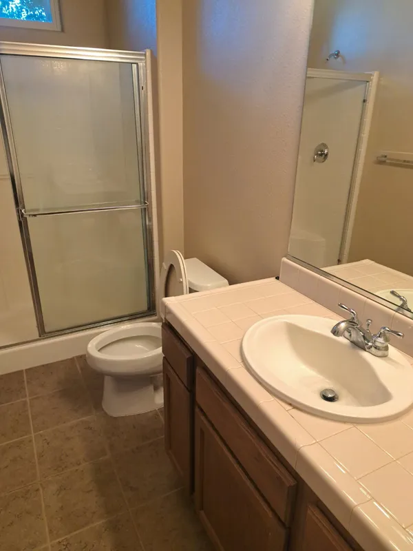 Bathroom with a glass shower door, toilet and tiled vanity